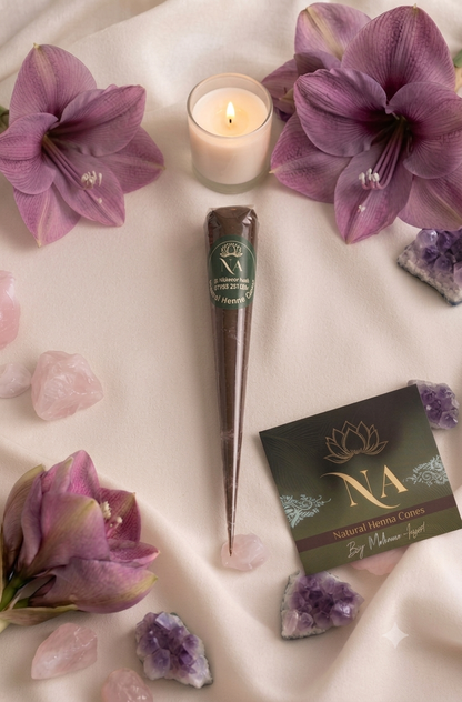 A set of brown cone-shaped incense sticks with green labels arranged in a fan shape on a draped cream fabric, surrounded by purple amaryllis, pink rose quartz, purple amethyst crystals, and a lit candle. A branded card for 'NA Natural Home Cares' is visible in the lower right.